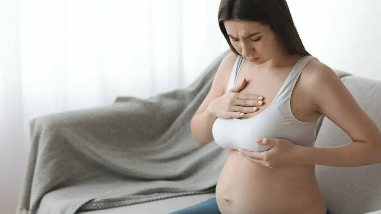 Ciężarna kobieta z bólem dotyka piersi, czując pierwsze oznaki siary.