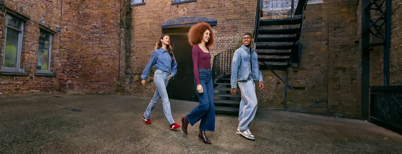 Three friends walk down an alleyway, showcasing how denim is breathable and stylish in various cuts and washes.