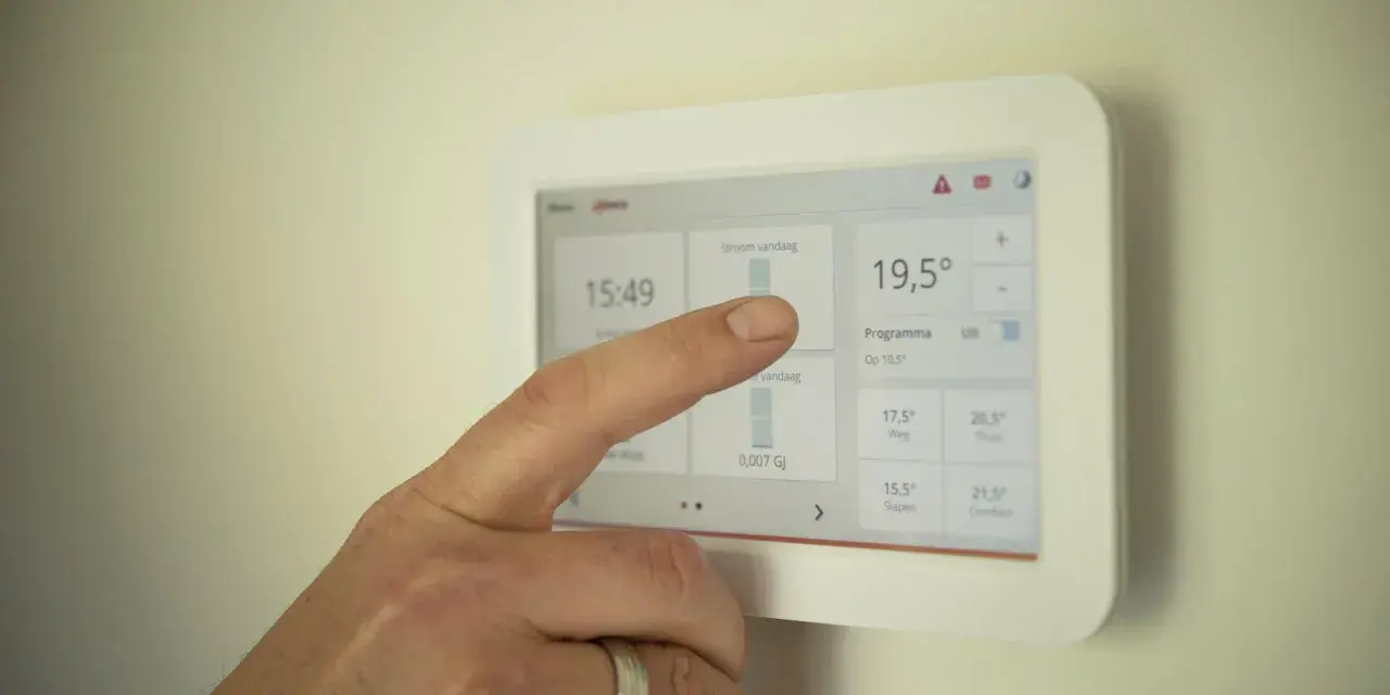 Un doigt interagit avec un écran tactile de domotique affichant la température et les programmes.
