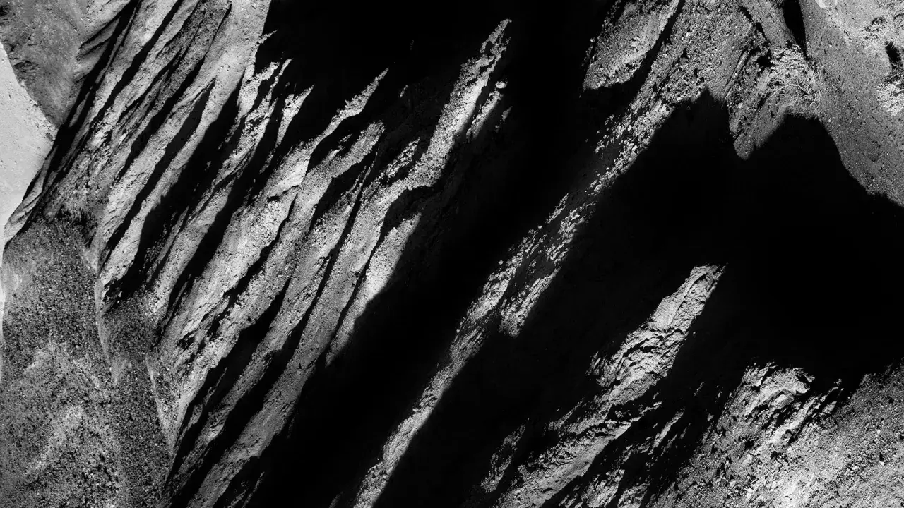 Abstract black and white landscape, reminiscent of Aaron Siskind photos, with dramatic shadows and textured rock formations.