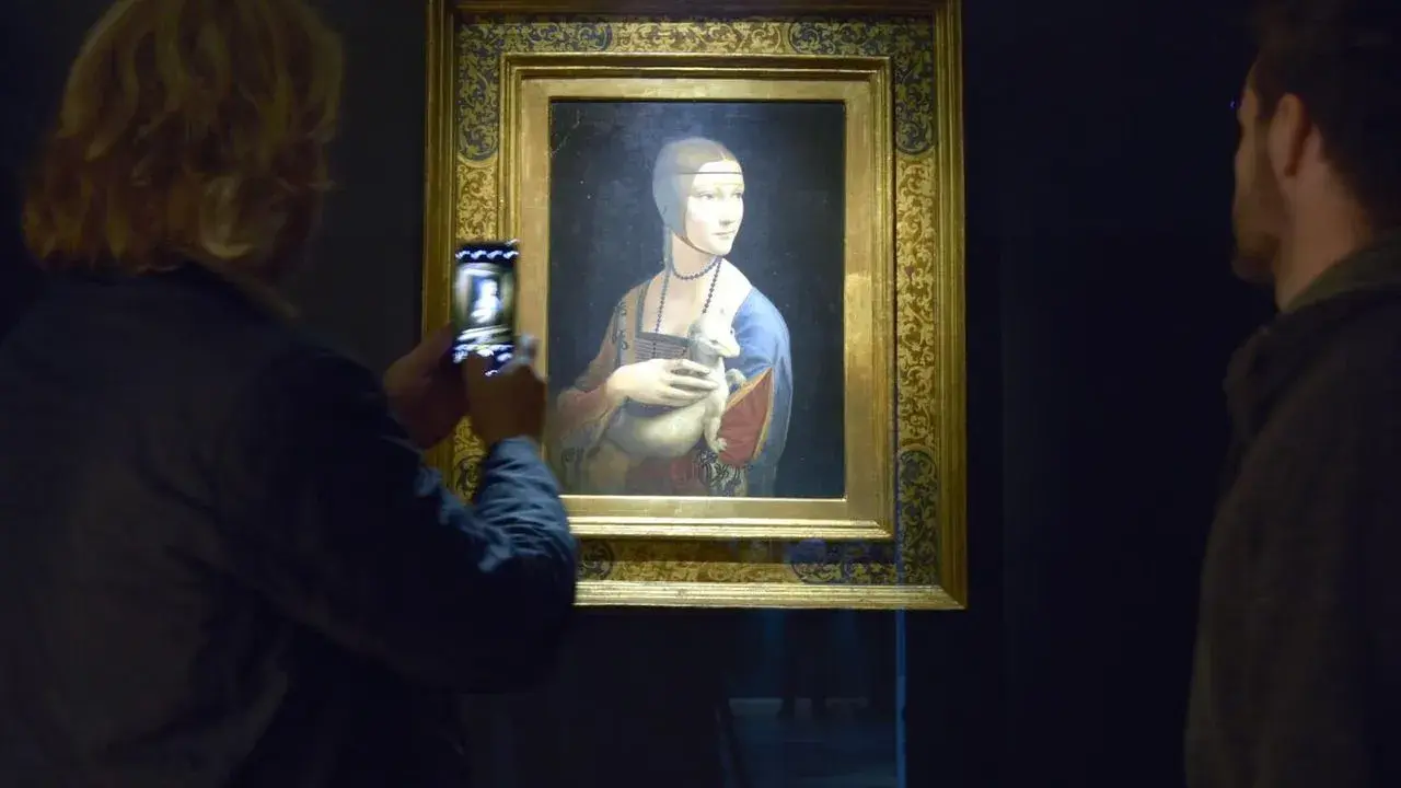 Dama z gronostajem Leonarda da Vinci, uwieczniona na zdjęciu przez turystkę. Obok obrazu stoi mężczyzna.