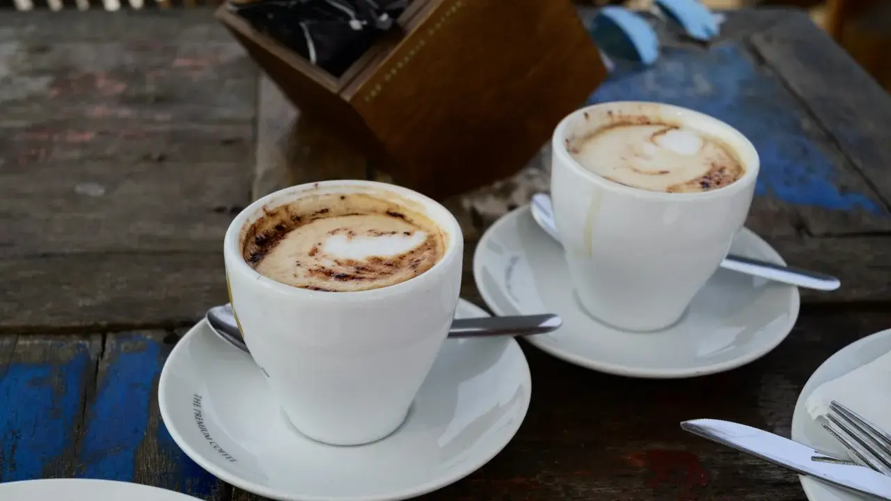 Zwei Tassen Kaffee Latte mit Milchschaum und Kakao-Muster auf einem Holztisch.
