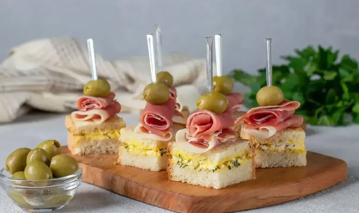 Eleganckie mini przekąski na imprezę: kanapki z szynką, jajkiem i oliwkami na wykałaczkach.