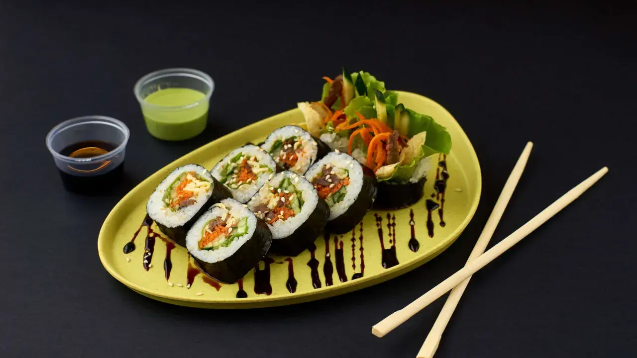 Kimbap-Röllchen mit Gemüse und Fleisch, serviert auf einem gelben Teller mit Sojasauce und Dip. Ein leckeres Kimbap Rezept zum Nachmachen.