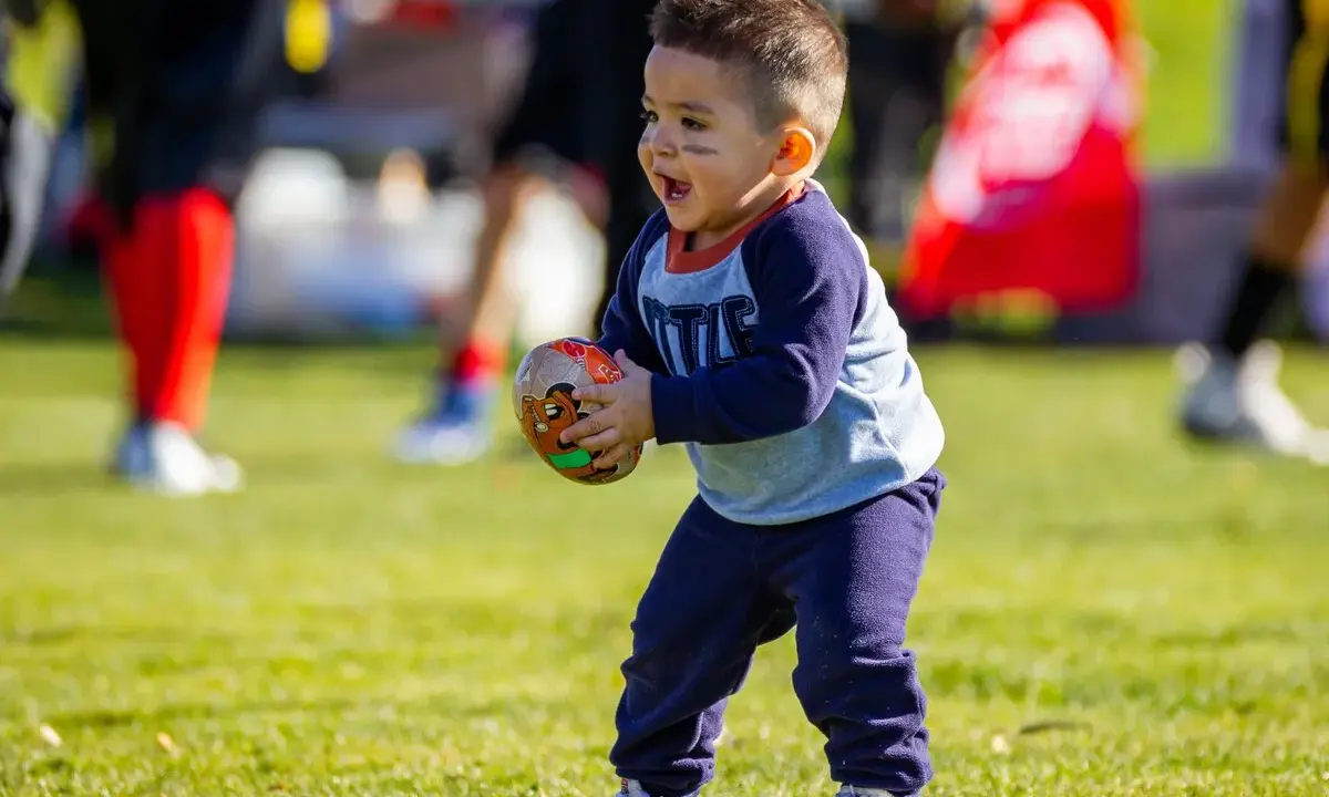 Niño feliz jugando con una pelota de fútbol americano, disfrutando de los juegos con pelotas para niños en un día soleado.