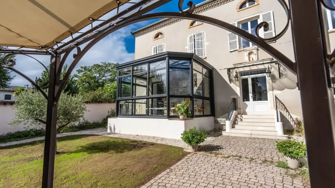 Une élégante véranda moderne s'intègre à une maison de campagne. La surface de plancher pavée mène à des marches menant à la porte d'entrée.