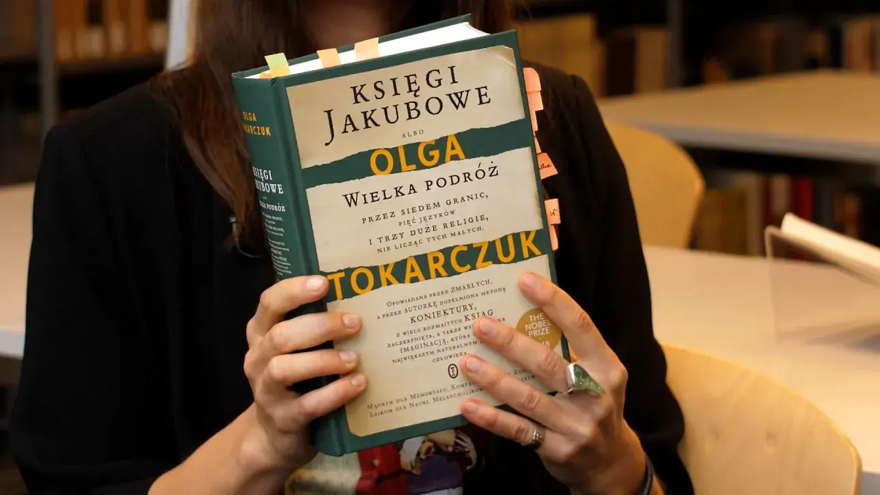 Osoba trzyma książkę "Księgi Jakubowe" Olgi Tokarczuk, z zakładkami w różnych kolorach.