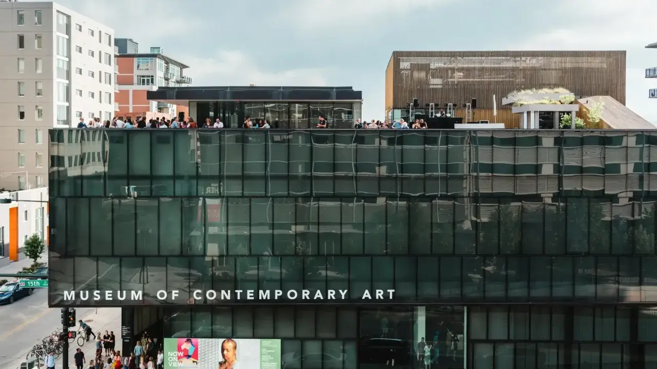People gather on the rooftop of the Museum of Contemporary Art Denver, enjoying the city views. Photos of the museum showcase its modern architecture.