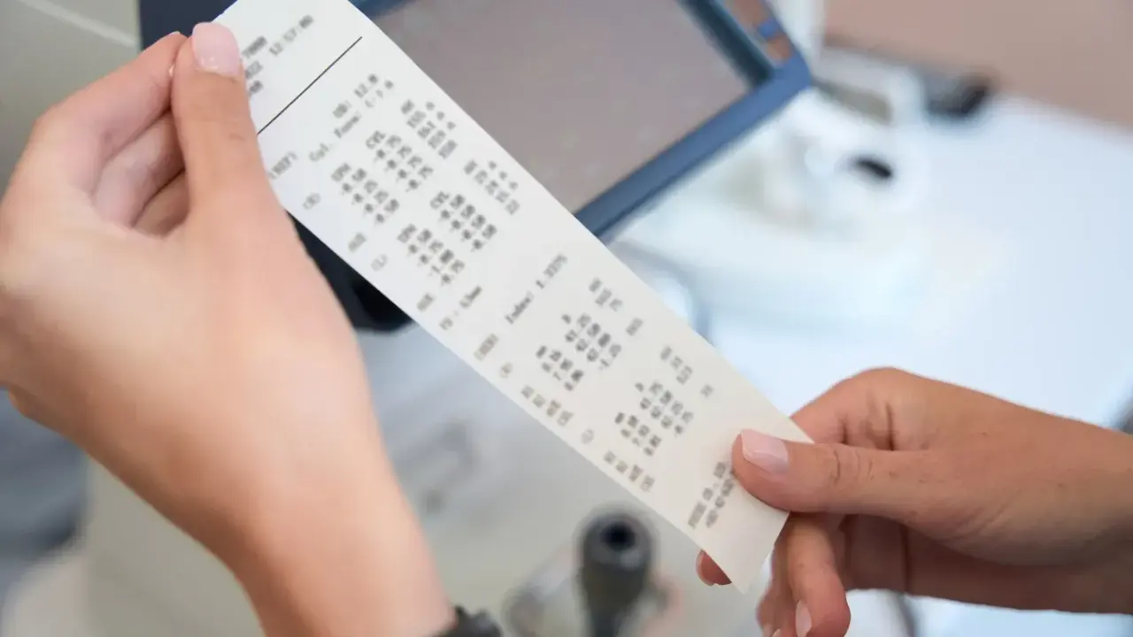 Dłonie trzymają wydruk z danymi optometrycznymi, gdzie widoczny jest numer paragonu.