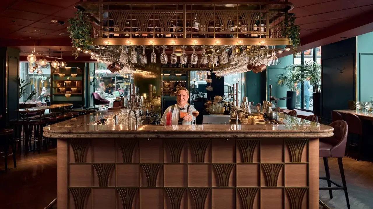 En glad bartender vid en elegant cocktail bar i Stockholm, med drinkar och glas på rad.
