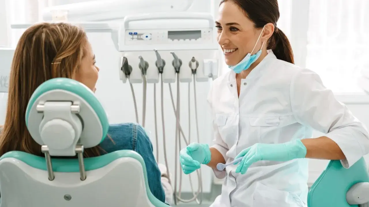 Uśmiechnięta dentystka w rękawiczkach rozmawia z pacjentką. Może właśnie omawia antybiotyk na zęba.