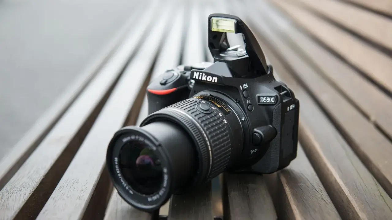 Czarny aparat Nikon D5600 z wysuniętą lampą błyskową leży na drewnianej ławce. Idealny do nikon d5600 test.