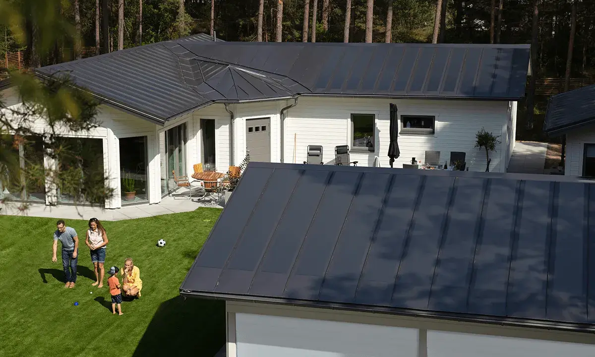 Familj njuter av solen på gräsmattan framför ett modernt hus med ett stilrent lindab solar roof.