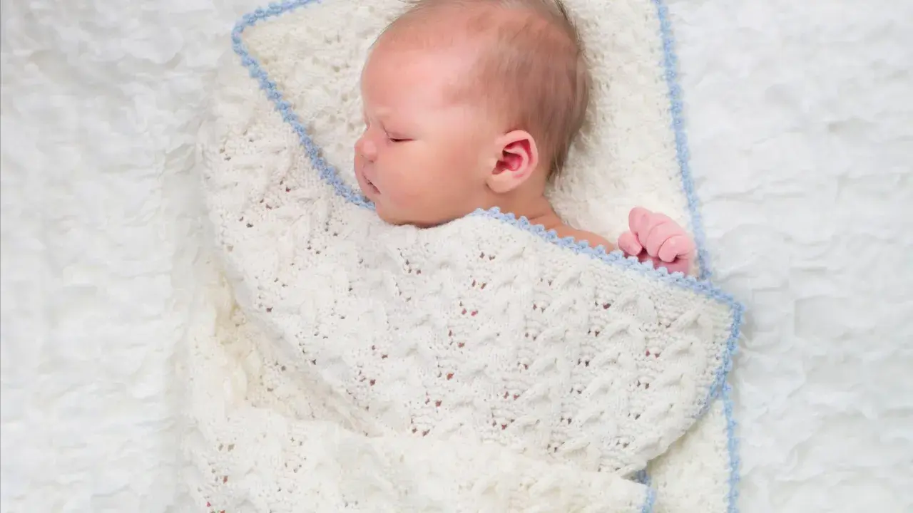 Sover sött i en stickad filt. Att knyta sjal bebis är ett mysigt sätt att hålla dem varma.