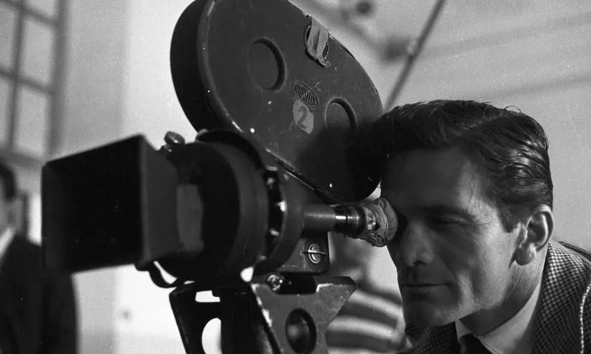 Pier Paolo Pasolini, con lo sguardo concentrato, osserva attraverso l'obiettivo di una cinepresa Arriflex, pronto a catturare la realtà.