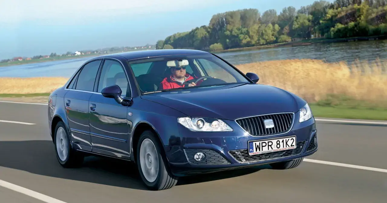 Granatowy Seat Exeo 2.0 TDI jedzie drogą nad rzeką, kierowca w czerwonej kurtce.