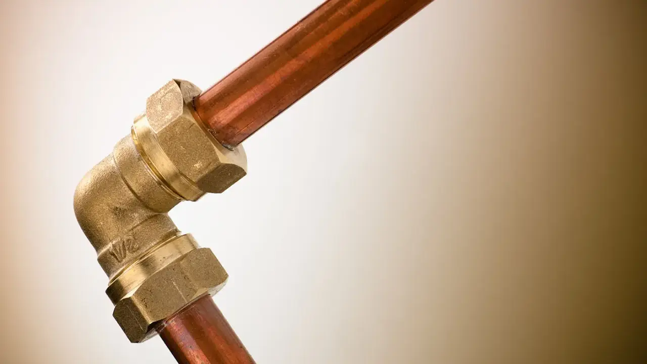 Un raccord coudé en laiton relie deux tuyaux en cuivre, illustrant une plomberie sans soudure efficace et durable.