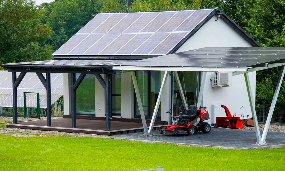 Maison moderne avec implantation panneau solaire sur le toit et le carport. Une tondeuse et un souffleuse à neige sont garés sous le carport.