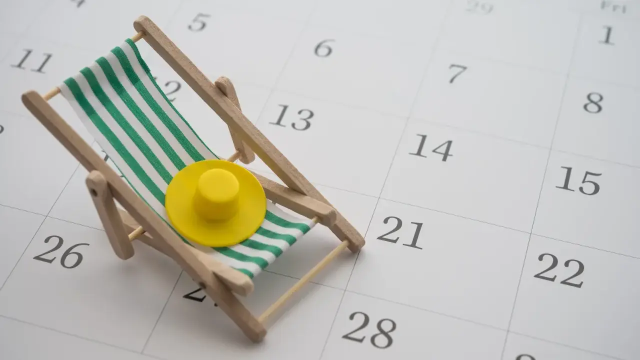 Miniaturowa leżanka plażowa z zielono-białymi pasami i żółtym kapeluszem na tle kalendarza.