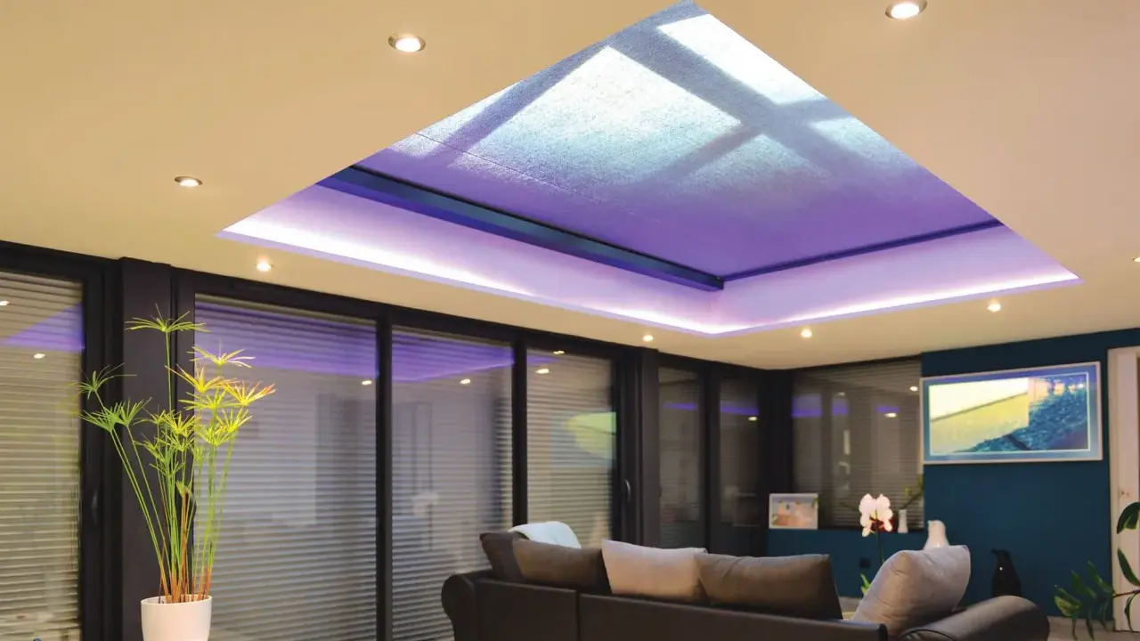 Salon moderne avec extension de maison et son puits de lumière illuminé de violet. Canapé confortable, plantes vertes et grandes baies vitrées.