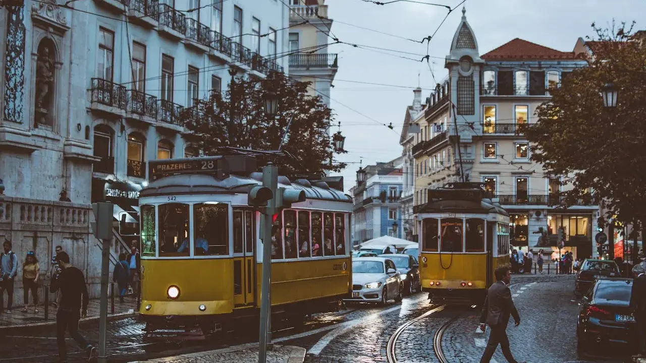 Lisbona, Portugalia. Żółte tramwaje na brukowanej ulicy, ludzie i samochody. Ceny w Portugalii mogą być różne, ale widok wart jest każdej ceny.