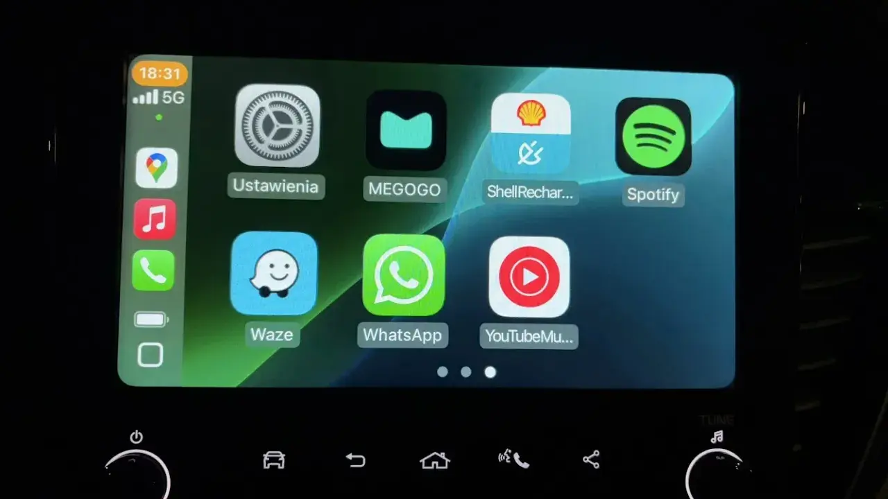 Ekran samochodu z ikonami aplikacji: Ustawienia, MEGOGO, Shell Recharge, Spotify, Waze, WhatsApp, YouTube Music. Działa system iOS CarPlay.