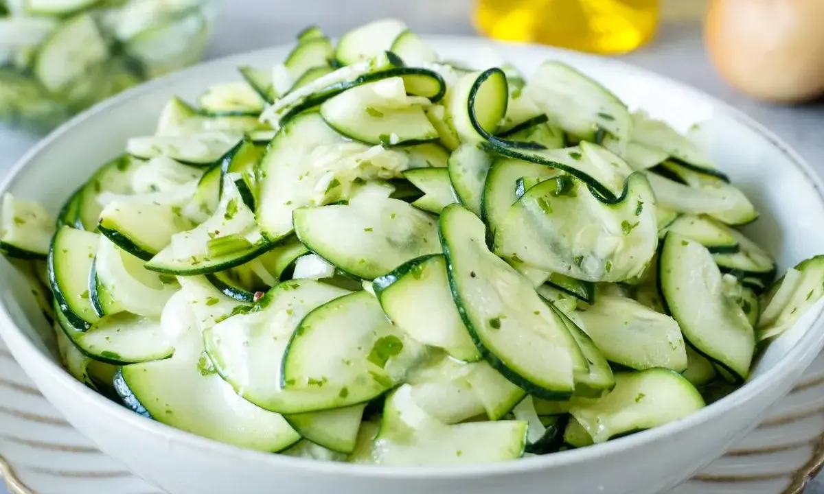 Frischer Salat aus dünn geschnittenen Zucchinischeiben, mariniert mit Kräutern und Öl. Perfekt, um Zucchini roh zu essen.