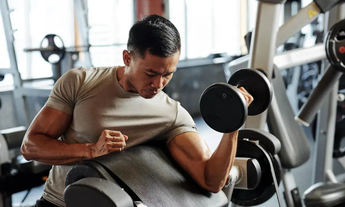 Mann trainiert Bizeps mit Kurzhantel. Fokus auf Muskelaufbau und Hypertrophie im Fitnessstudio.