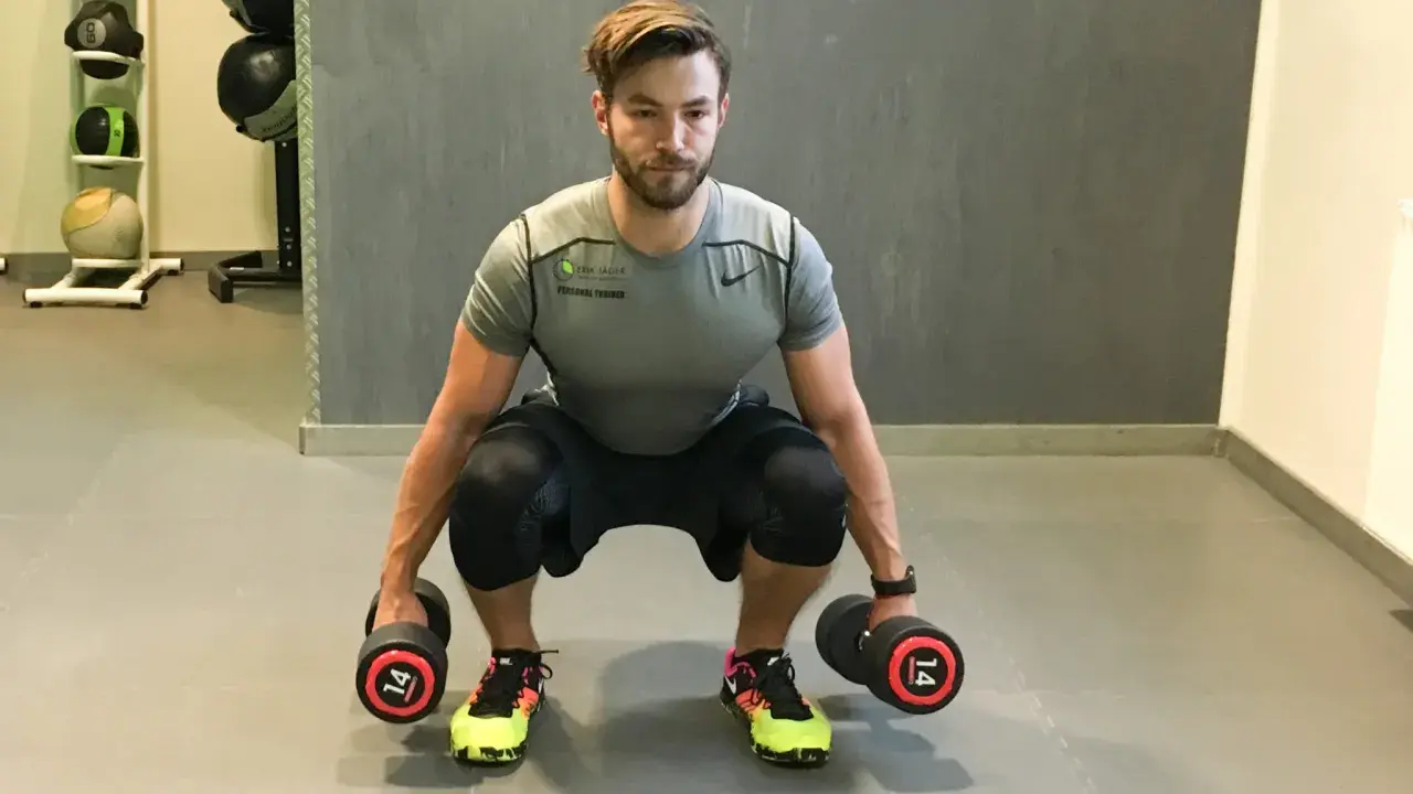 Mann macht Kniebeugen mit Kurzhanteln. Er hält zwei Hanteln mit je 14 kg Gewicht.