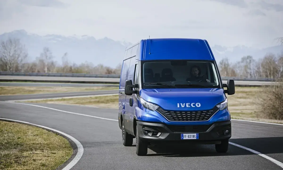Niebieski Iveco Daily 3 na zakręcie drogi, z kierowcą za kierownicą. W tle góry i drzewa.