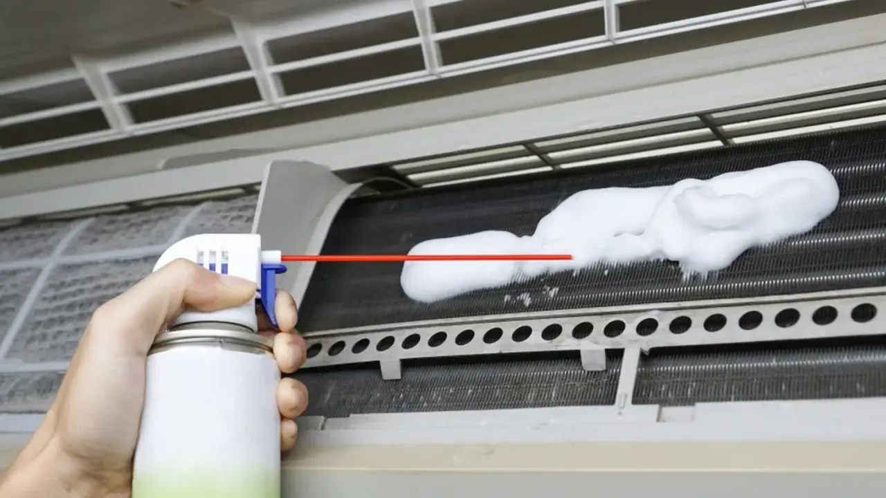 Mano rociando espuma para limpiar aire acondicionado unidad interior.
