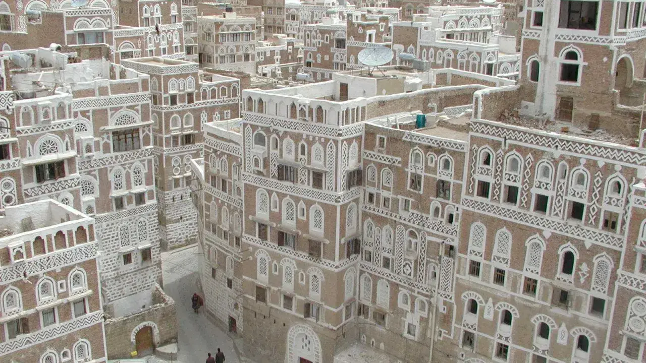 Ein malerisches arabisches Haus mit kunstvollen weißen Verzierungen und vielen Fenstern, eingebettet in eine Stadt mit ähnlicher Architektur.