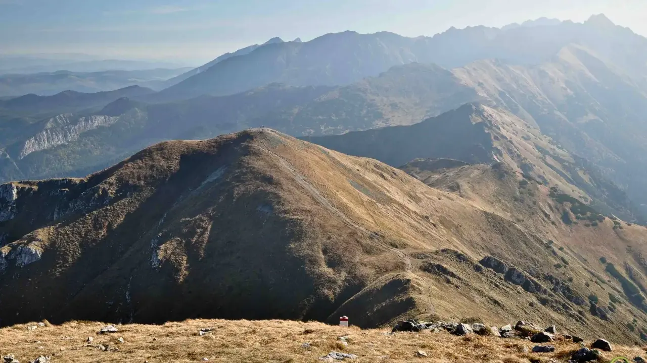 Widok na pasmo górskie Tatr. W oddali widać kolejne grzbiety górskie, a na pierwszym planie ścieżki i kamienie. Trasy Tatry zachęcają do wędrówki.