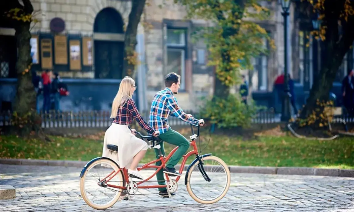 Para co to? Para na rowerze typu tandem przemierza brukowaną uliczkę w jesiennym mieście.