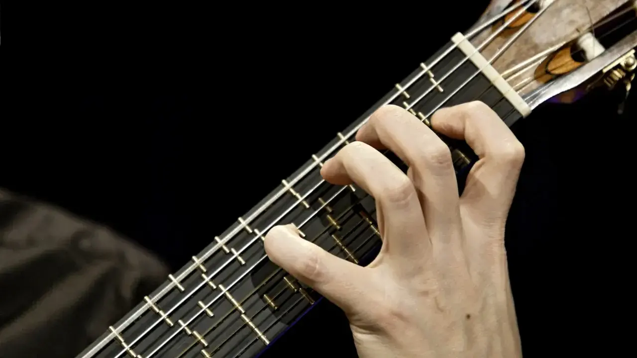 Main d'un guitariste jouant sur une microtonal guitar, ses doigts effleurant les cordes sur un manche sombre.