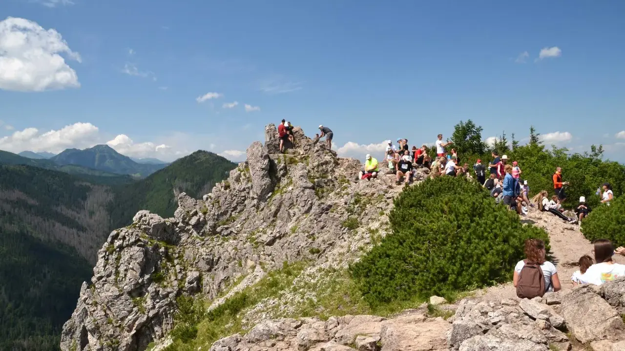 Grupa turystów odpoczywa na skalistym szczycie, podziwiając widok na dolinę. Białe chmury na niebie sugerują, że do szczytu było niedaleko.