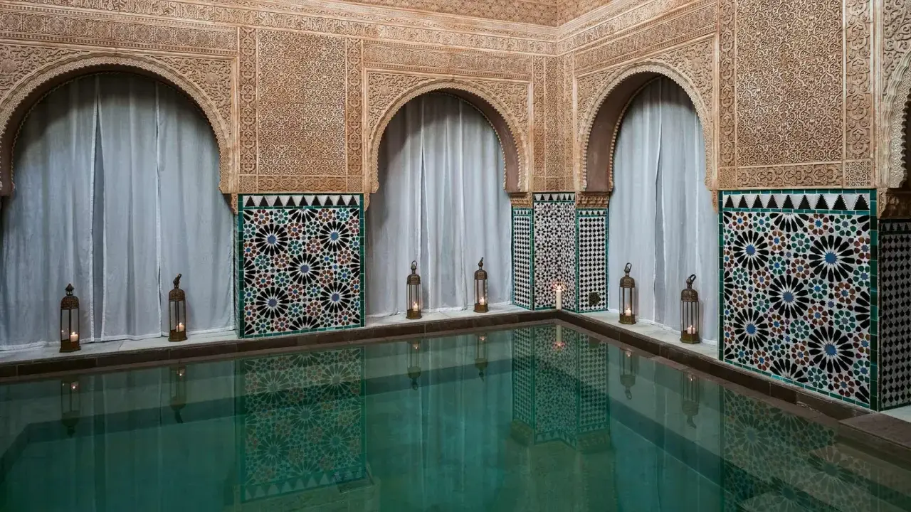 Ein ruhiger Pool im Hammam Al Andalus, umgeben von kunstvollen Fliesen und Schnitzereien, mit Kerzenlicht.