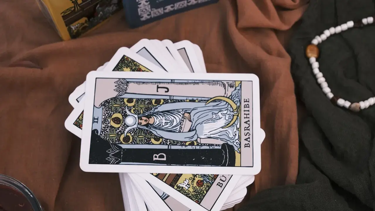 Karty tarota ułożone na brązowym materiale. Jedna karta, przedstawiająca postać z księżycem i owocami, jest na wierzchu. To idealny obrazek na **tarot na tydzień**.