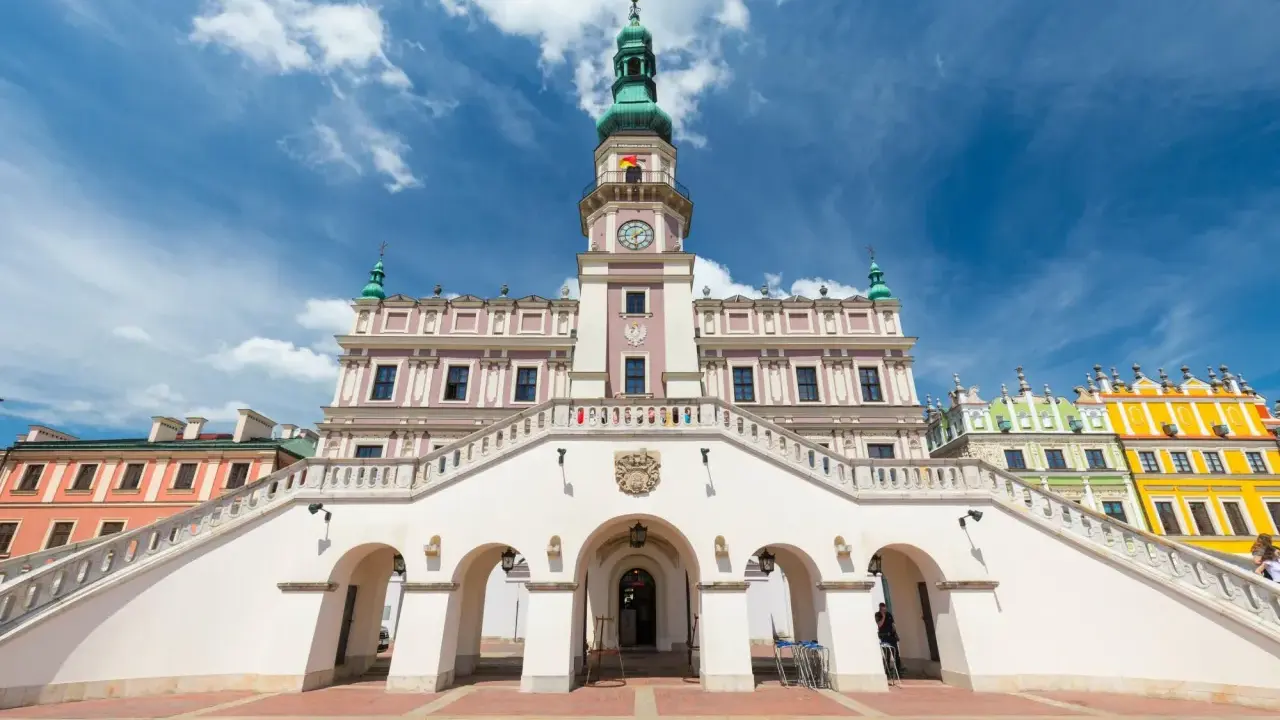 Zamość rynek: Ratusz z imponującymi schodami i kolorowe kamienice pod błękitnym niebem.