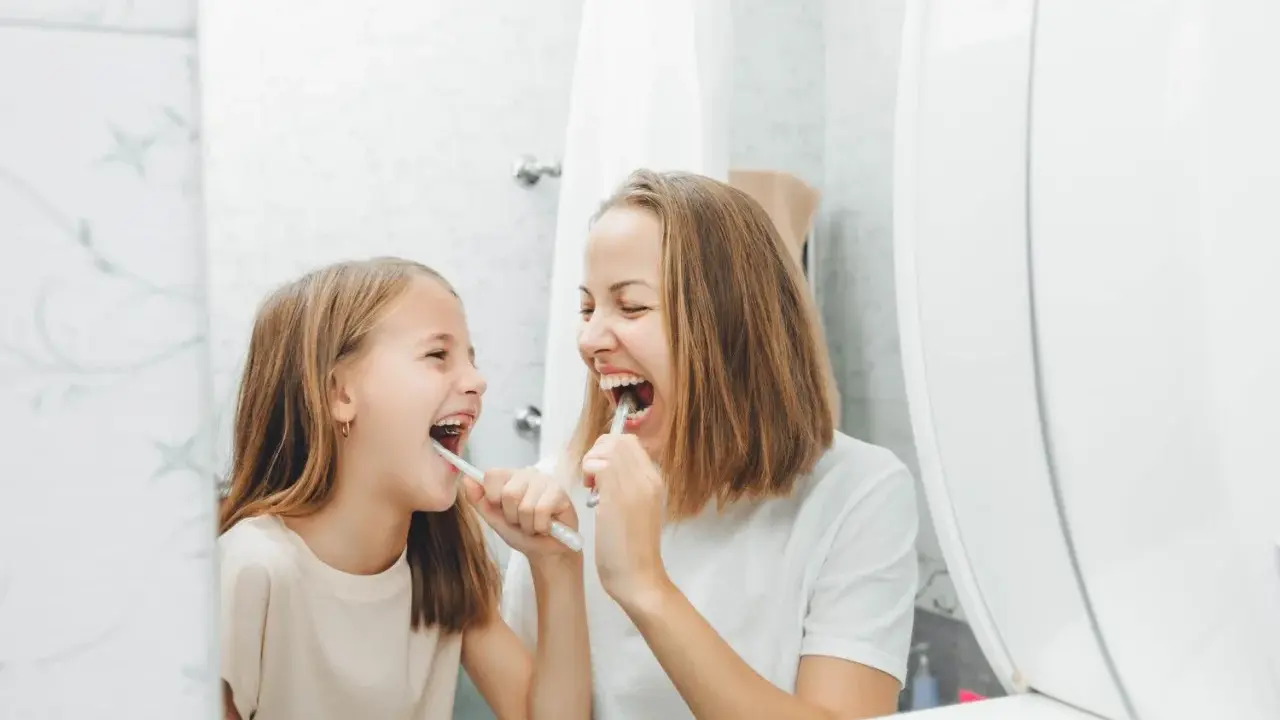 Mama i córka myją zęby, śmiejąc się. Dziecko nie chce myć zębów, ale mama przekonuje je zabawą.