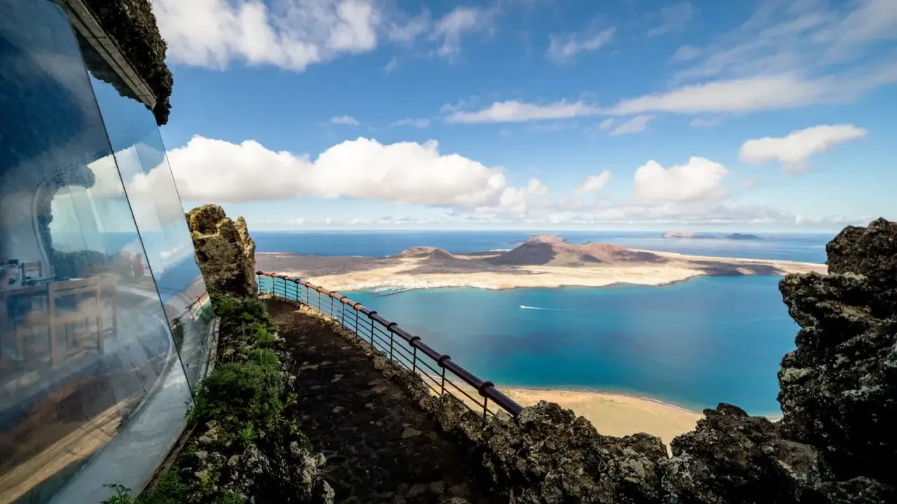 Blick vom Mirador del Río auf das Tal der tausend Palmen Lanzarote. Blaue See, Inseln und eine Hütte mit Glasfront.