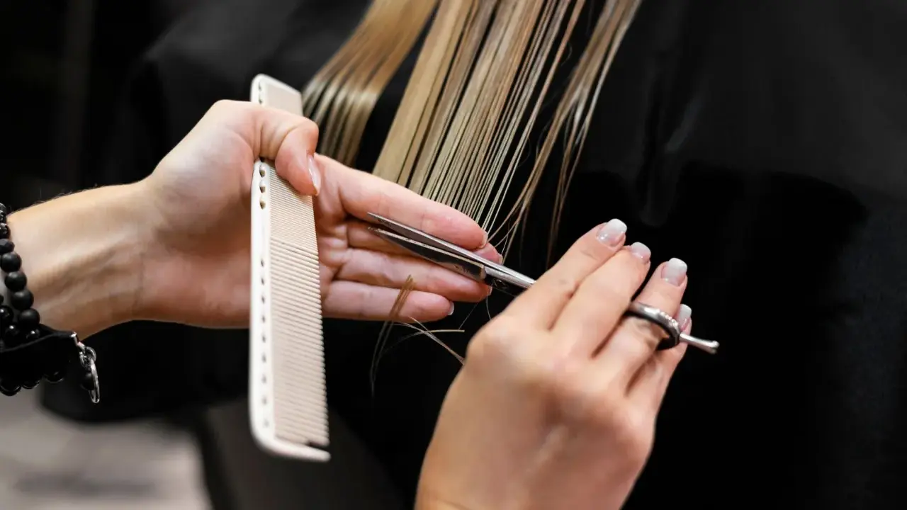 Manos de estilista cortando cabello rubio con tijeras y peine. Decisión: cortar el pelo en seco o mojado.
