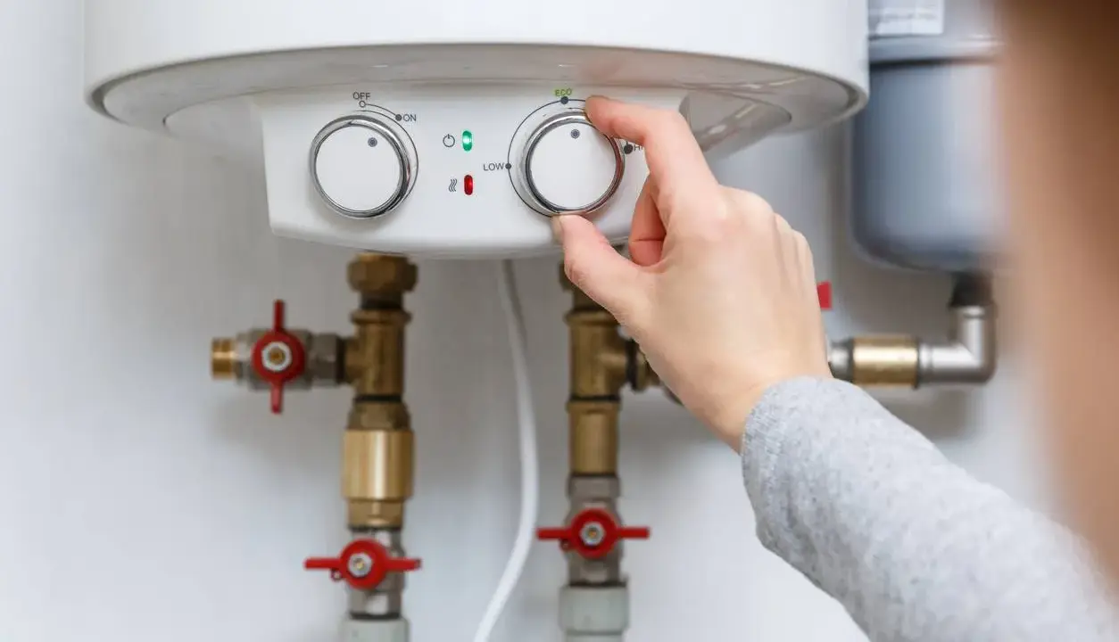 Main d'une personne ajustant le thermostat d'un chauffe-eau, contrôlant la pression de l'eau et la température.