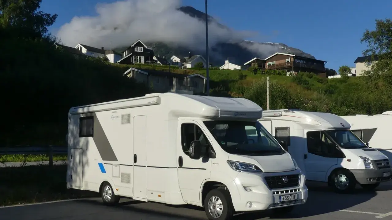 Husbil parkerad vid Trollstigen i Norge. Husen klättrar uppför den gröna sluttningen mot molnen.