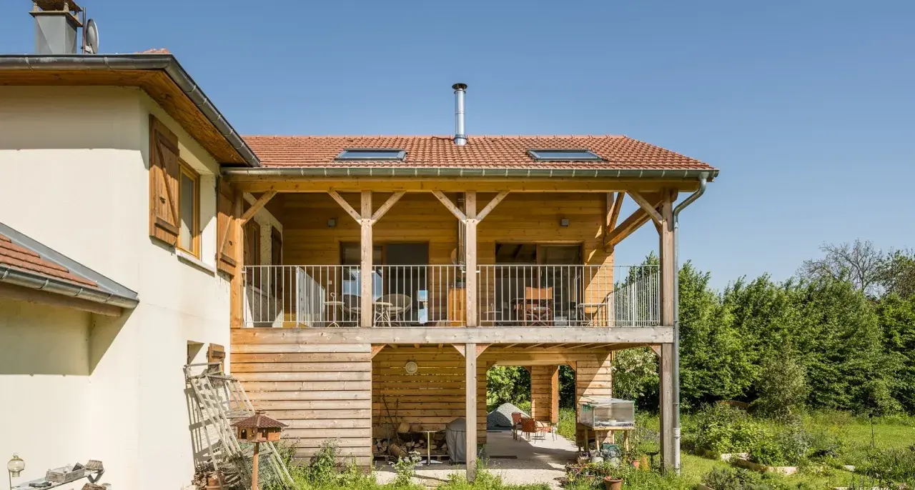 Extension en bois sur pilotis, avec balcon et terrasse aménagée. Une belle intégration architecturale.