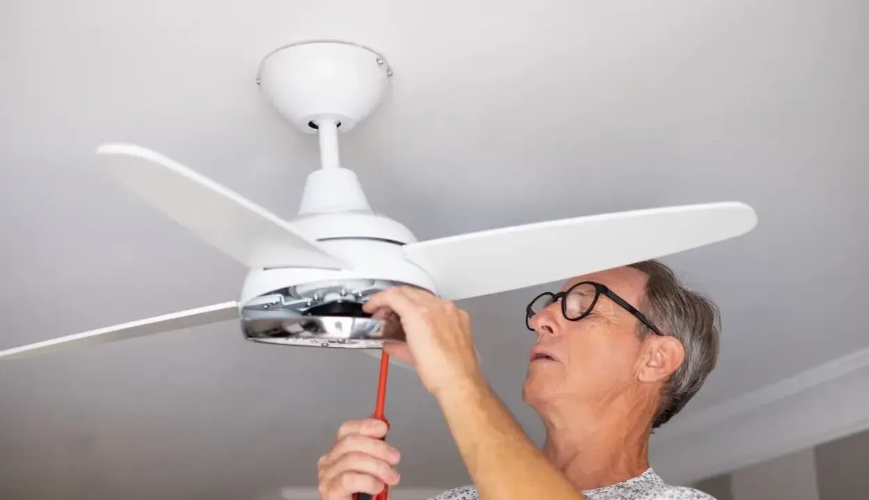 Hombre con gafas ajusta un ventilador de techo pladur con un destornillador.