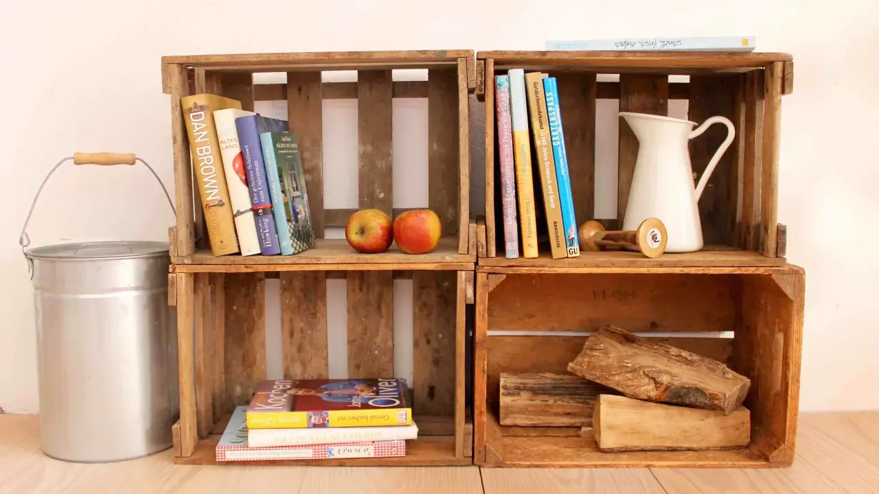 Alte Weinkisten-Ideen: Bücher, Äpfel, eine Kanne und Holzscheite schaffen rustikales Flair.