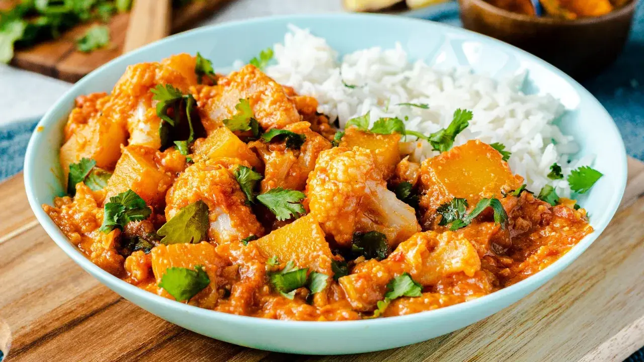 Herzhaftes Aloo Gobi mit Blumenkohl und Kartoffeln in würziger Tomatensauce, garniert mit Koriander und serviert mit Reis.