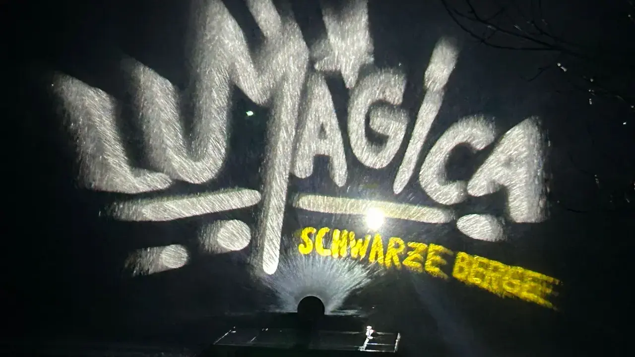 LUMAGICA Schwarze Berge Schriftzug auf Wasserprojektion bei Nacht.