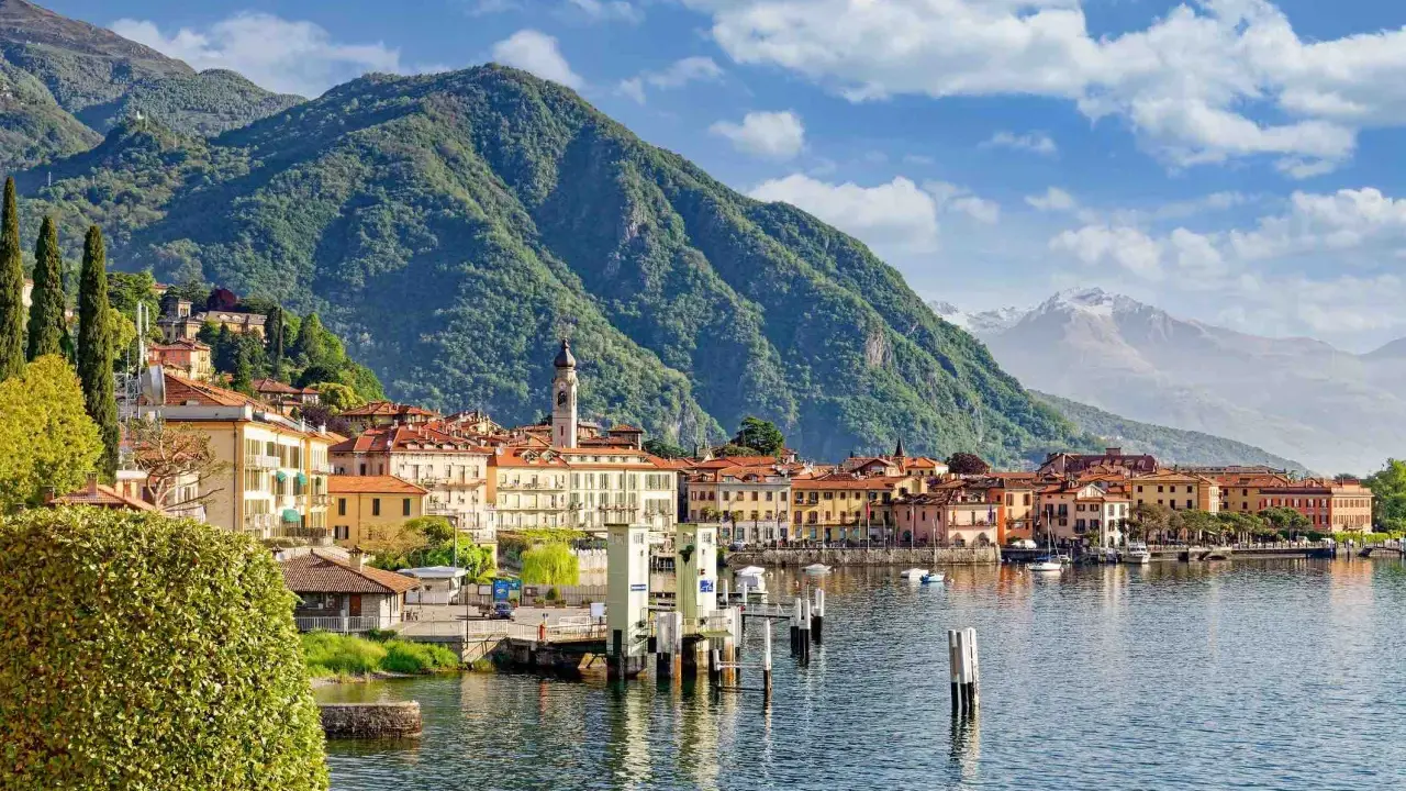 Vista di un paese sul lago d'Iseo, con montagne verdi sullo sfondo. La profondità del lago d'Iseo è suggerita dalla vastità dell'acqua.